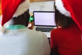 Happy diverse couple wearing santa claus hats, using laptop with copy space Royalty Free Stock Photo