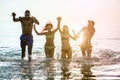 Happy diverse culture friends having fun inside water on the beach - Young people dancing and jumping in sea with back sun light Royalty Free Stock Photo