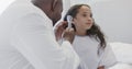 Happy diverse doctor examining sick girl patient with otoscopy in hospital in slow motion