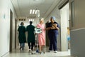 Happy diverse female doctor and senior female patient with iv pole talking in busy hospital corridor Royalty Free Stock Photo