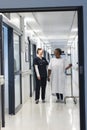 Happy diverse female doctor talking with senior female patient with drip in hospital corridor Royalty Free Stock Photo