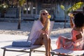 Happy diverse female friends having party by swimming pool, sitting on deck chairs and drinking beer Royalty Free Stock Photo