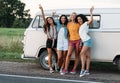 Happy diverse friends at camper van. Four smiling women standing together on the roadside near a car during vacation Royalty Free Stock Photo