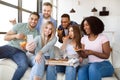Happy diverse friends having party, sitting on sofa with pizza, chips and cellphone, socializing at home