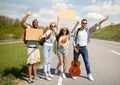 Happy diverse friends standing on highway with empty sign, waving down car, going on journey together, outdoors Royalty Free Stock Photo