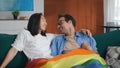 Happy diverse gay couple holding rainbow flag symbol of lgbt and relaxing together on sofa. Royalty Free Stock Photo