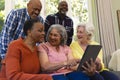 Happy diverse group of senior friends using tablet and laughing in sunny living room Royalty Free Stock Photo
