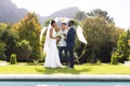 Happy diverse male officiant, bride and groom at outdoor wedding ceremony by pool in sunny garden Royalty Free Stock Photo