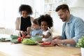 Happy diverse parents with adorable daughters preparing meal together