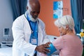 Happy diverse senior male doctor taking blood pressure of senior female patient, copy space Royalty Free Stock Photo