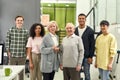 Happy diverse team of employees smiling at camera while posing with senior female and male interns, standing together in Royalty Free Stock Photo