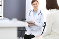 Happy doctor and patient discussing something while sitting at the chairs at hospital. Physician at work in clinic