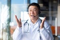 Happy doctor smiles and looks at the camera, Asian announces good news to the patient, uses a video call, and a headset online