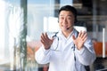 Happy doctor smiles and looks at the camera, Asian announces good news to the patient, uses a video call, and a headset online