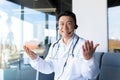 Happy doctor smiles and looks at the camera, Asian announces good news to the patient, uses a video call, and a headset online