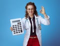 Happy doctor woman with big white calculator showing ok on blue