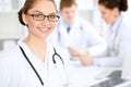 Happy doctor woman with medical staff at the hospital sitting at the table. Red frame glasses Royalty Free Stock Photo