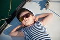 Happy smiling caucasian kid in captain white hat stripe tank top and sunglasses lying relaxing on luxury sea yacht during summer Royalty Free Stock Photo