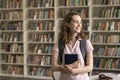 Happy dreamy student girl with backpack posing in campus library