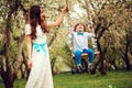 Happy dressy mother and toddler child son having fun on swing in spring or summer park