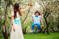 Happy dressy mother and toddler child son having fun on swing in spring or summer park
