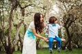 Happy dressy mother and toddler child son having fun on swing in spring or summer park, wearing bow tie and long lacy dress for bi Royalty Free Stock Photo