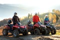 Happy drivers in protective helmets enjoying extreme riding on ATV quad motorbikes in summer mountains at sunset