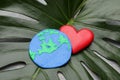 Happy Earth Day. Planet made of plasticine and decorative heart on green leaf, closeup