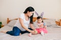 Happy Easter. Asian Chinese pregnant mother with baby girl playing with colorful Easter eggs on a bed at home. Kid child and