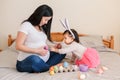 Happy Easter. Asian Chinese pregnant mother with baby girl playing with colorful Easter eggs on a bed at home. Kid child and