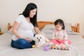 Happy Easter. Asian Chinese pregnant mother with baby girl playing with colorful Easter eggs on a bed at home. Kid child and