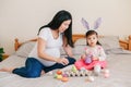 Happy Easter. Asian Chinese pregnant mother with baby girl playing with colorful Easter eggs on a bed at home. Kid child and