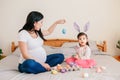 Happy Easter. Asian Chinese pregnant mother with baby girl playing with colorful Easter eggs on a bed at home. Kid child and