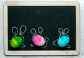 Happy Easter card background - three colorful, pastel Easter eggs with painted rabbit ears against the background of a blackboard Royalty Free Stock Photo