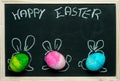 Happy Easter card background - three colorful, pastel Easter eggs with painted rabbit ears against the background of a blackboard Royalty Free Stock Photo