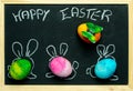 Happy Easter card background - three colorful, pastel Easter eggs with painted rabbit ears against the background of a blackboard Royalty Free Stock Photo