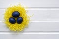 Happy easter card - place for text. Blue easter eggs in a yellow nest on a white wooden background, selective focus Royalty Free Stock Photo