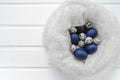 Happy easter card - place for text. Blue easter and quail eggs in a snow-white woolen cozy nest on a white wooden background, Royalty Free Stock Photo