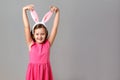 Happy easter. Cheerful little girl in a pink dress with polka dots on a gray background. The child holds his hands behind the Royalty Free Stock Photo