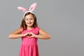 Happy easter. Cheerful little girl in a pink dress with polka dots on a gray background. A child in a rabbit costume shows a heart Royalty Free Stock Photo