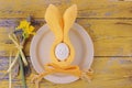 Easter holiday table setting with cutlery on barn boards. Narcissus, rubbit from egg and yellow napkin with bow on white Royalty Free Stock Photo