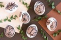 Happy Easter concept. Surreal faces on eggs and green branches of eucalyptus on brown background. Art und Online style