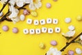 Happy Easter. Cubes with text on yellow background. Spring brunches with white flowers and candy, chocolate easter eggs.