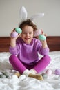 Happy Easter. cute beautiful girl with curly hair and bunny ears sitting on the bed with colorful easter eggs. Lifestyle photo Royalty Free Stock Photo