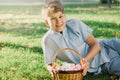 Happy Easter! Cute smiling boy teenager in blue shirt holds basket with handmade colored eggs on grass in spring park. Decoration Royalty Free Stock Photo