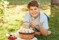 Happy Easter! Cute smiling boy teenager in blue shirt holds basket with handmade colored eggs on grass in spring park Royalty Free Stock Photo
