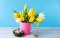 Happy Easter. Decorative easter eggs in bird nest and bouquet of yellow tulips in bucket on blue background. Concept: beautiful Royalty Free Stock Photo