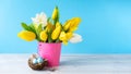 Happy Easter. Decorative easter eggs in bird nest and bouquet of yellow tulips in bucket on blue background. Concept: beautiful Royalty Free Stock Photo