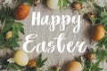Happy Easter greeting card. Happy Easter text sign handwritten on  Easter eggs and spring flowers frame on rustic linen, flat lay Royalty Free Stock Photo