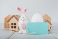 Happy Easter greeting card. Miniature wooden house. Rabbits, colorful eggs, spring flowers with tag for text Royalty Free Stock Photo